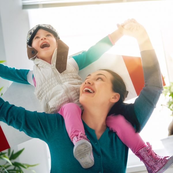 Happy family is having fun at home. Mother and her child girl playing together. Girl in pilot's costume.